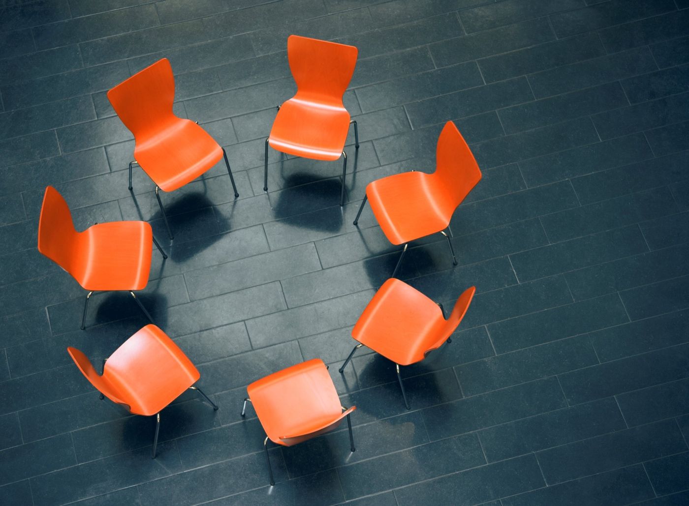 Empty orange chairs arranged in a circle on a dark floor